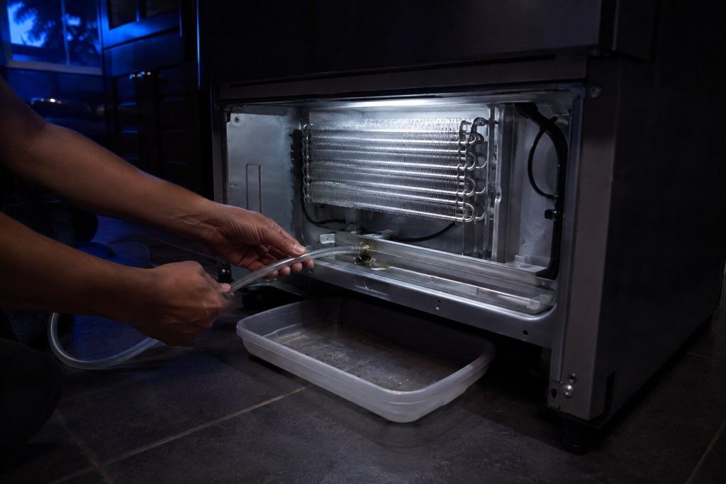 A length of flexible tubing being fed into the drain trough at the bottom of an evaporator compartment ... a shallow tray under the machine.